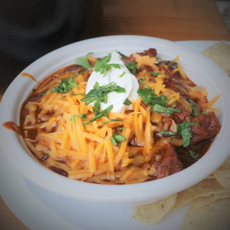 A bowl of smoked chili topped with shredded cheese, sour cream, and cilantro.