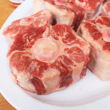 Raw oxtail sitting on a white plate.