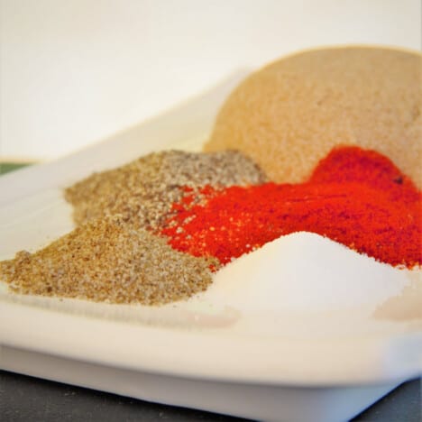 Piles of the herbs and spices used to make the rub sit on a white plate.
