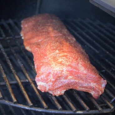 A rack of pork ribs sits on a smoker.