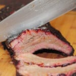 The cooked pork ribs being sliced with a knife on a wooden cutting board.