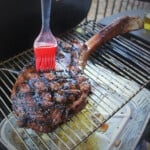 A red basting brush rubbing a basting sauce onto the cooked tomahawk steak.