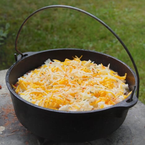 A cast iron Dutch oven holds a finished cottage pie with plenty of shredded cheese on top.