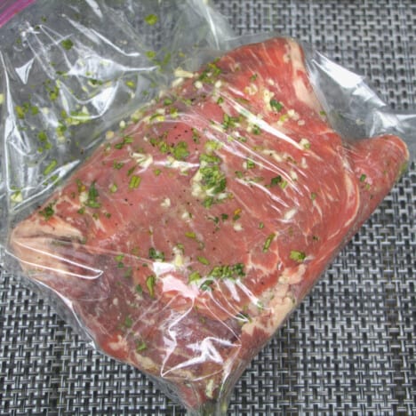 Flank steak in a plastic bag being marinated with finely diced garlic and herbs.