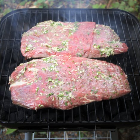 The raw but marinated steaks cooking on a hot charcoal grill.