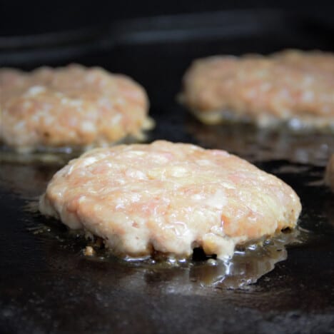 Three Hawaiian pork burgers are cooking on a griddle.