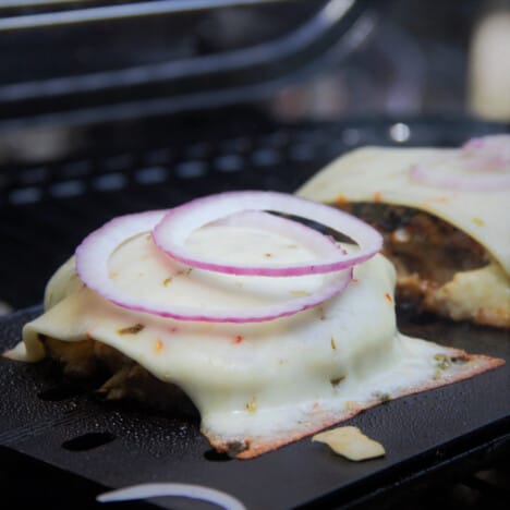 A close up shot of a Hawaiian pork burger smothered in melted cheese and topped with red onions.