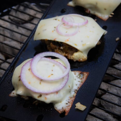 Looking down onto cooked Hawaiian pork burgers with melted cheese and sliced red onions.