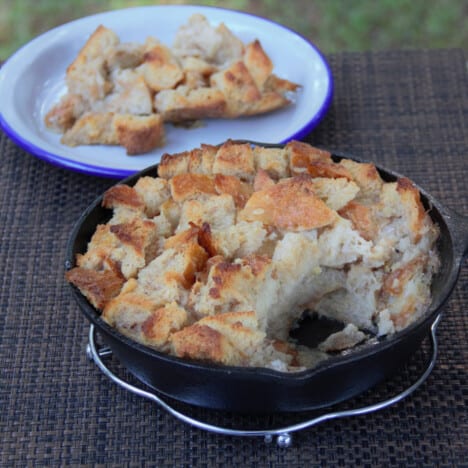 Bananas Foster bread pudding in skillet with a serving from it sitting behind on a white shallow plate.