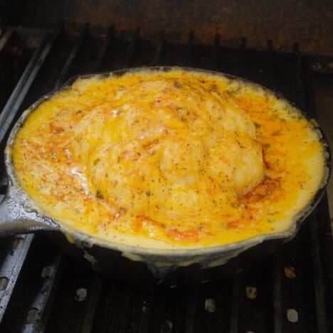 Looking down into a cast iron skillet with a head of cauliflower covered in a cheesy bechamel sauce.
