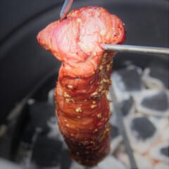 A cooked char siu still hanging in the round drum smoker ready to be removed.