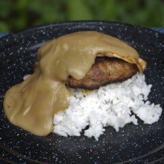A black camp plate with a layer of rice topped with a meat patty, fried egg, and gravy.