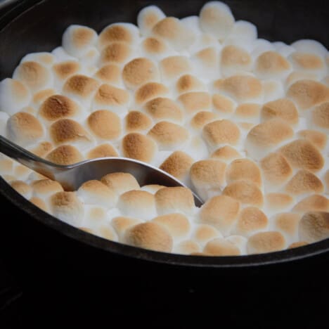 A spoon taking out the first serving of a golden marshmallow topped sweet potato casserole.