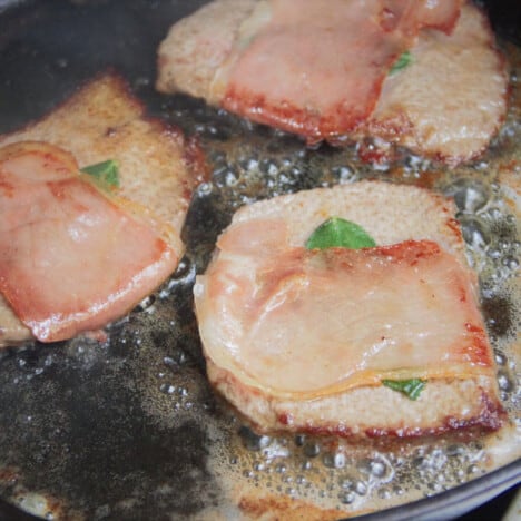 Prosciutto-wrapped veal steaks with sage frying in a pan.