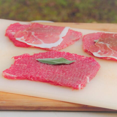 Raw veal steaks pounded thin on a cutting board.