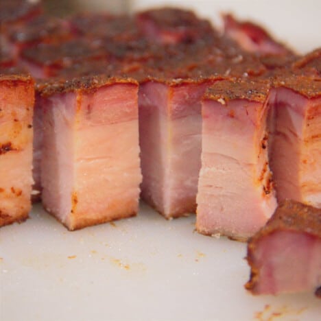 Looking into slices of cooked pork belly on a white cutting board.