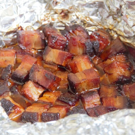 Browned cubes of pork belly sitting in liquid in foil.