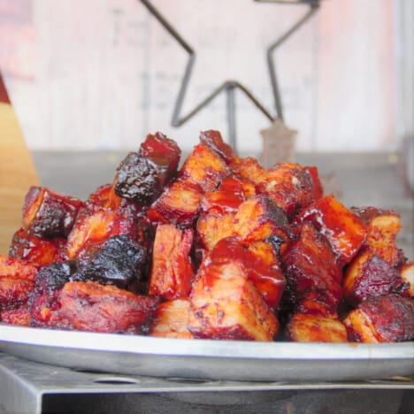 A stack of candied pork belly cubes served on a white plate.