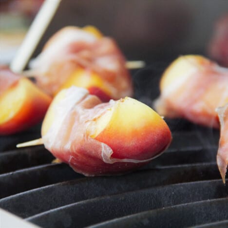 Closeup of a prosciutto-wrapped peach cooking on a grill.