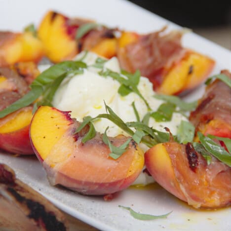 Grilled prosciutto-wrapped peaches served on a platter with mascarpone and greens.
