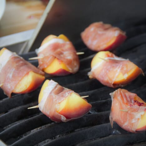 A grill top covered in prosciutto-wrapped peaches cooking.