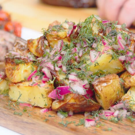 A platter of Grilled Potato Salad garnished with extra dill and chopped red onions.