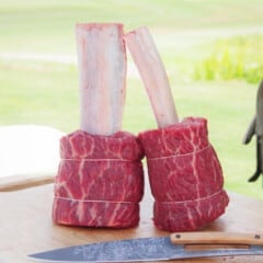 Two prepared beef rib pops standing on a chopping board.