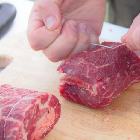 A piece of butcher's twine being tied around the meat of the rib to help it stay in place.