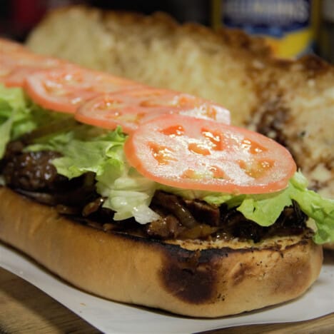 An open brisket po'boy sandwich topped with shredded lettuce and sliced tomatoes.