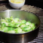 A stainless frypan on a grill cooking brussels sprouts.
