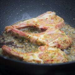 Three lamb cutlets covered in a whole grain mustard slather cooking in a frypan.