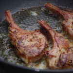 Three golden brown lamb cutlets in a frypan.