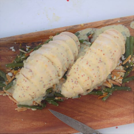 Two chicken breasts served sliced on a wooden chopping board covered in a white wine and mustard sauce.