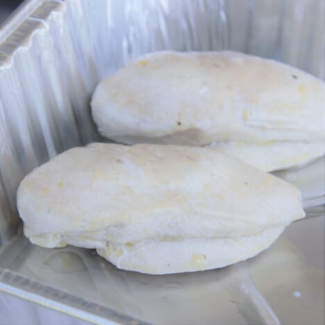 Two cooked chicken breasts awaiting serving in a foil pan.