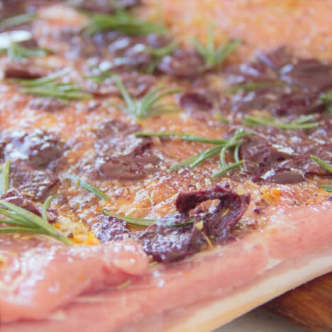 A pork belly is laid out with the filling of olives, rosemary, and orange zest spread evenly over it.