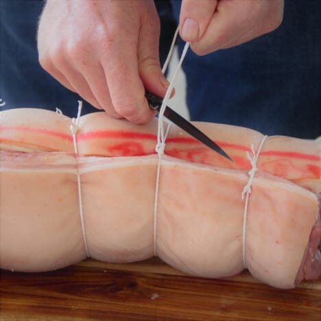 A piece of butcher's twine is being trimmed after being tied to secure the porchetta.