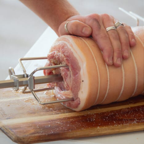 A stuffed and tied raw prochetta is having the spit and spit prongs added ready to be cooked.