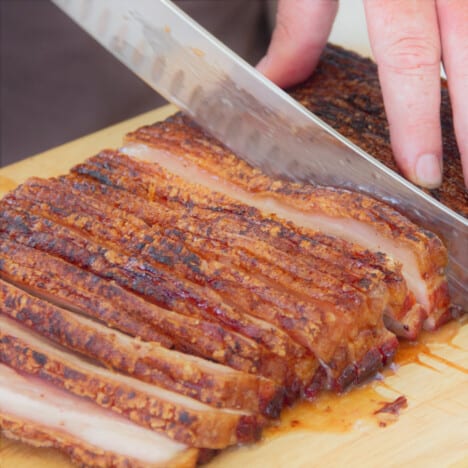 Thinly slicing the roasted pork belly on a wooden chopping board.