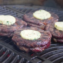 Four Scotch steaks on a grill with a slice of compound butter on them.