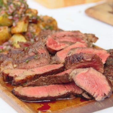 A wooden serving platter with sliced rump steak and a grilled potato salad.