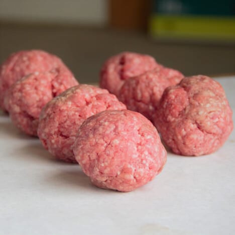 Six balls of ground beef sit on a work surface, waiting to be cooked.