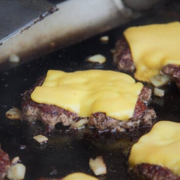 A close up of a smash burger topped with melted American cheese on a flat-top grill.