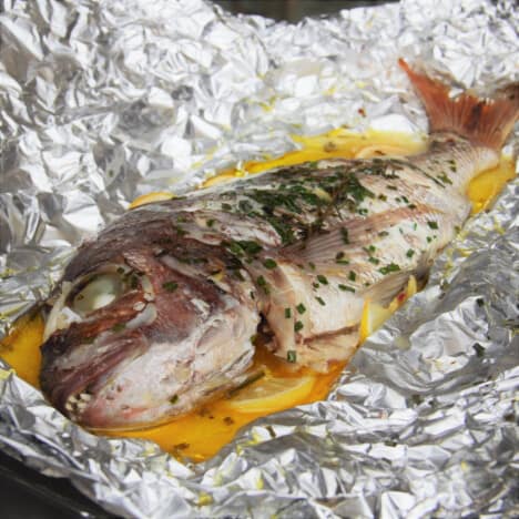 Unwrapped foils exposes a baked snapper sitting on a bed of lemons.