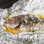 Opened foil exposing the cooked snapper sitting on a bed of lemons.