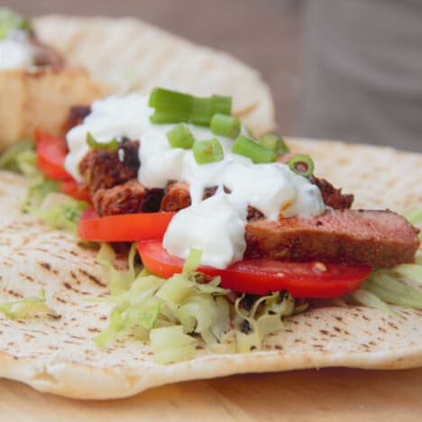 A pita bread topped with lettuce, tomato, lamb and tzatziki.