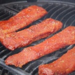Four bright red lamb backstraps cooking on a grill.