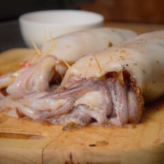 Two stuffed squid, with toothpicks holding the tentacles in place, are resting on a wooden cutting board.