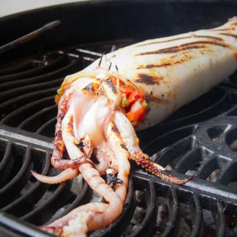 An almost fully cooked chorizo-stuffed squid sitting on a grill.
