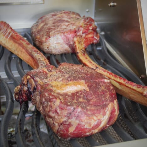 Two tomahawk steaks on a cool grill to start cooking.