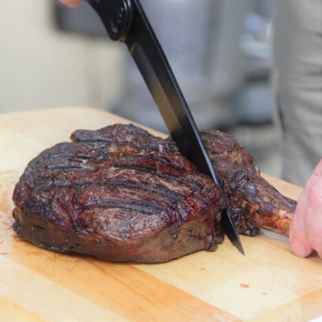 The bone being cut away from the meat of the cooked tomahawk steak.